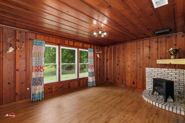 unfurnished living room featuring hardwood / wood-style floors, a wood stove, wooden walls, and wood ceiling