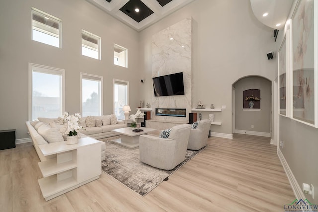 living room with a fireplace, a towering ceiling, coffered ceiling, and light hardwood / wood-style flooring