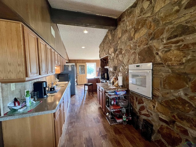 kitchen featuring white oven, lofted ceiling with beams, stainless steel fridge, dark wood-type flooring, and a textured ceiling