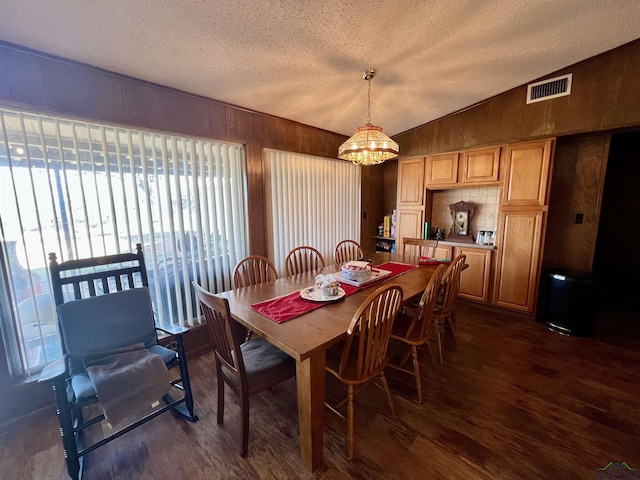 dining space with a textured ceiling, lofted ceiling, wood walls, dark hardwood / wood-style floors, and a notable chandelier