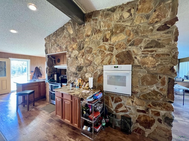 interior space featuring stainless steel electric stove, white oven, beamed ceiling, wooden walls, and a textured ceiling