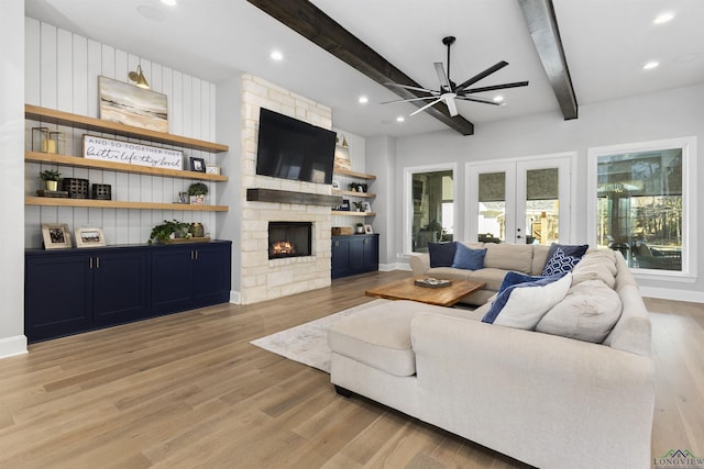 living room featuring light hardwood / wood-style floors, beam ceiling, french doors, and a stone fireplace