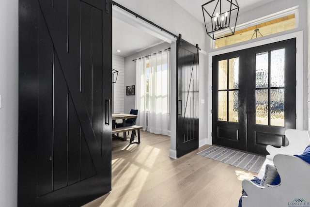 entryway with a barn door, french doors, a chandelier, and light hardwood / wood-style flooring