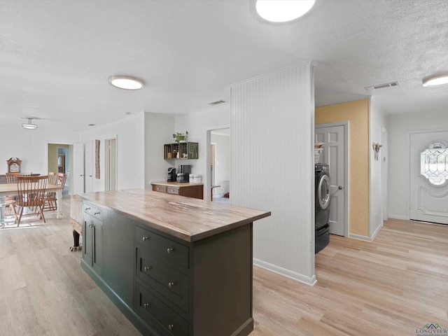 kitchen with light wood-type flooring, washer / dryer, a center island, and wooden counters