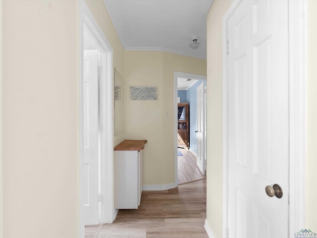 hallway with light wood-type flooring and ornamental molding