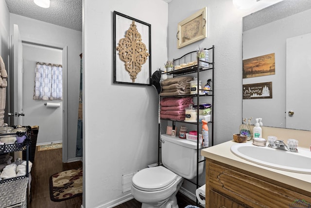 bathroom featuring baseboards, toilet, vanity, wood finished floors, and a textured ceiling