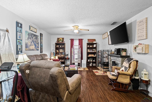 living area featuring visible vents, a ceiling fan, a textured ceiling, wood finished floors, and a stone fireplace