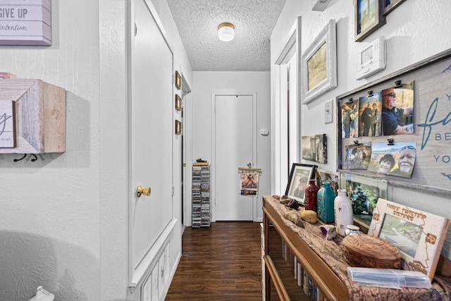 hallway featuring visible vents, a textured ceiling, and dark wood finished floors