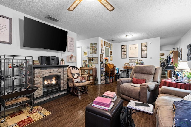 living area with wood finished floors, visible vents, ceiling fan, a stone fireplace, and a textured ceiling