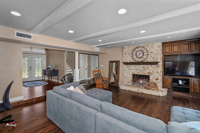 living room with french doors, a textured ceiling, beamed ceiling, dark hardwood / wood-style floors, and a stone fireplace