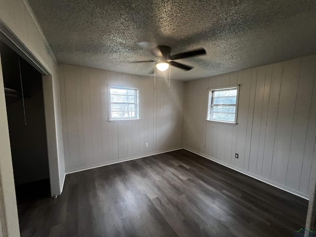 unfurnished bedroom with ceiling fan, a closet, dark hardwood / wood-style floors, and wooden walls