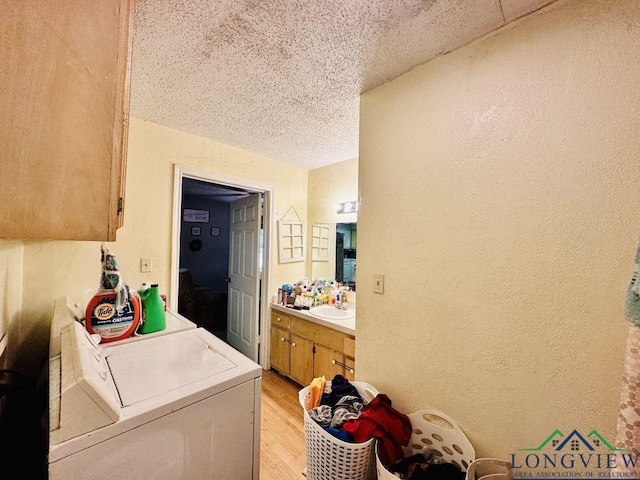 washroom featuring a textured ceiling, light wood-type flooring, sink, and washing machine and clothes dryer