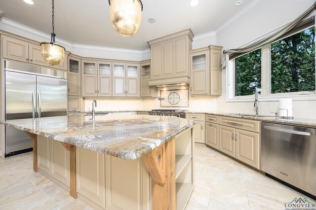 kitchen featuring light stone counters, appliances with stainless steel finishes, decorative light fixtures, and a kitchen island with sink