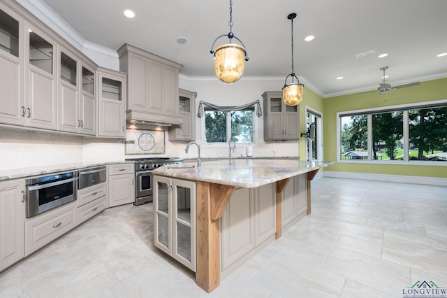 kitchen featuring stainless steel stove, decorative light fixtures, a breakfast bar area, light stone countertops, and a center island with sink