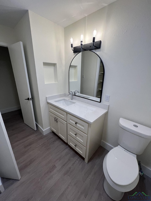 bathroom featuring toilet, wood finished floors, vanity, and baseboards