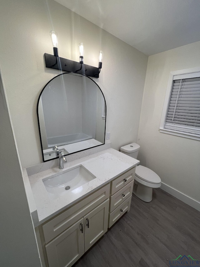 bathroom featuring toilet, baseboards, wood finished floors, and vanity