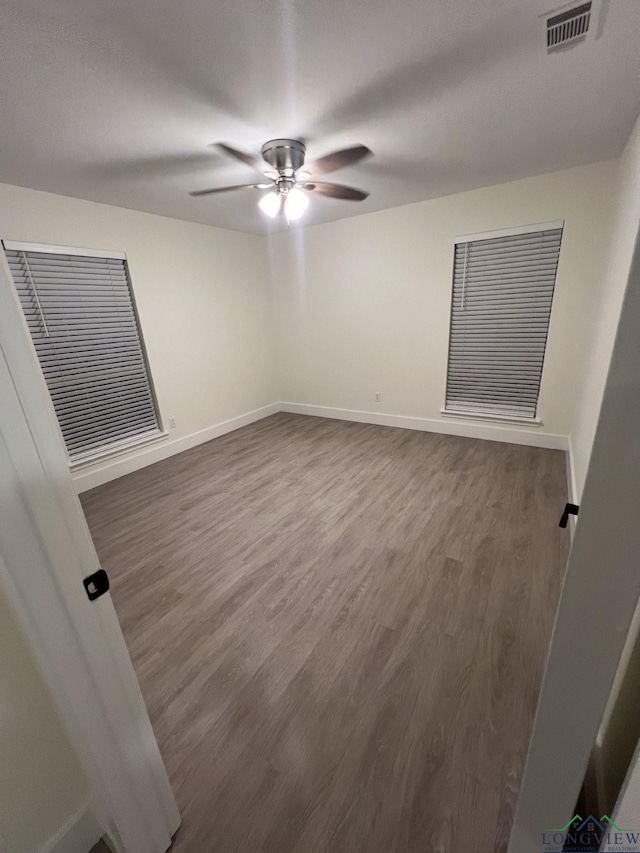 unfurnished room featuring dark wood-style flooring, visible vents, ceiling fan, and baseboards