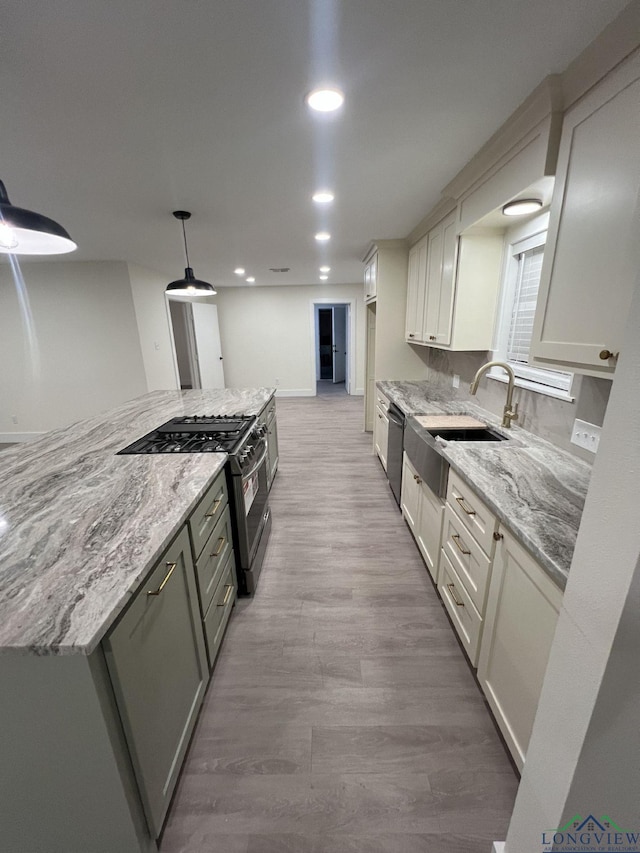 kitchen with light stone counters, a sink, dishwasher, light wood finished floors, and gas stove