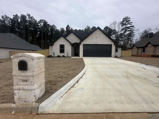 french country style house with concrete driveway, an attached garage, and fence