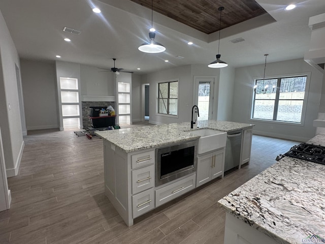 kitchen with decorative light fixtures, appliances with stainless steel finishes, open floor plan, white cabinetry, and an island with sink