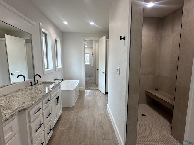 bathroom with a walk in shower, wood finished floors, vanity, baseboards, and a soaking tub