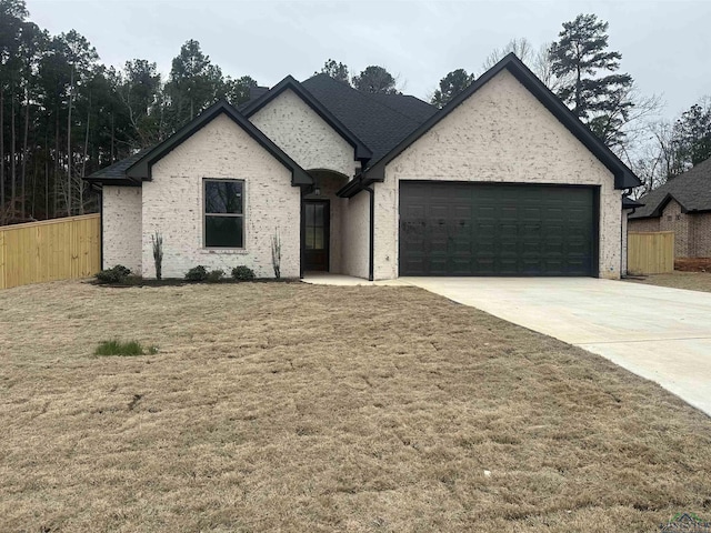 french country style house featuring a garage, brick siding, fence, concrete driveway, and a front lawn