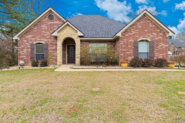 view of front of house with stone siding, a shingled roof, a front lawn, and brick siding