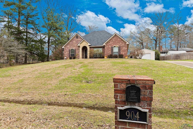 view of front facade featuring a shingled roof, fence, an outdoor structure, a front lawn, and brick siding