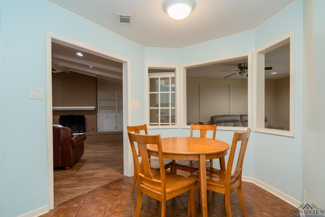 dining area with dark tile patterned flooring, ceiling fan, lofted ceiling, and a brick fireplace