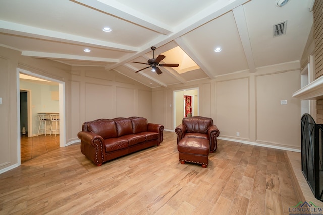 living room featuring vaulted ceiling with beams, light hardwood / wood-style flooring, a brick fireplace, and ceiling fan