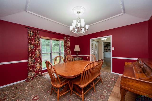 dining area featuring a raised ceiling, hardwood / wood-style floors, vaulted ceiling, and an inviting chandelier