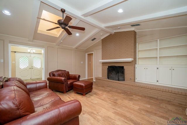 living room featuring lofted ceiling with beams, light wood-type flooring, ceiling fan with notable chandelier, and a brick fireplace