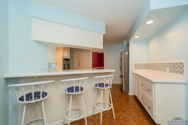 kitchen with backsplash, kitchen peninsula, a kitchen bar, and appliances with stainless steel finishes