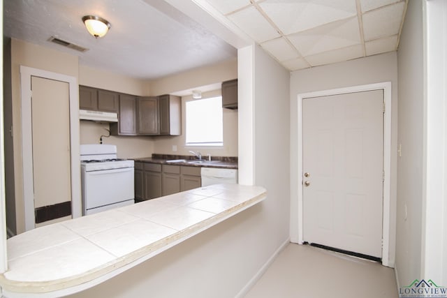 kitchen with dark brown cabinetry, white appliances, tile counters, and kitchen peninsula