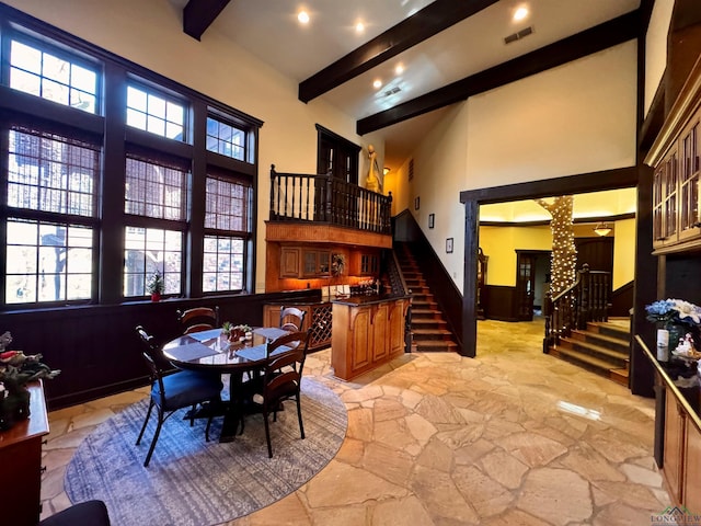 dining area with beam ceiling, indoor bar, plenty of natural light, and a high ceiling