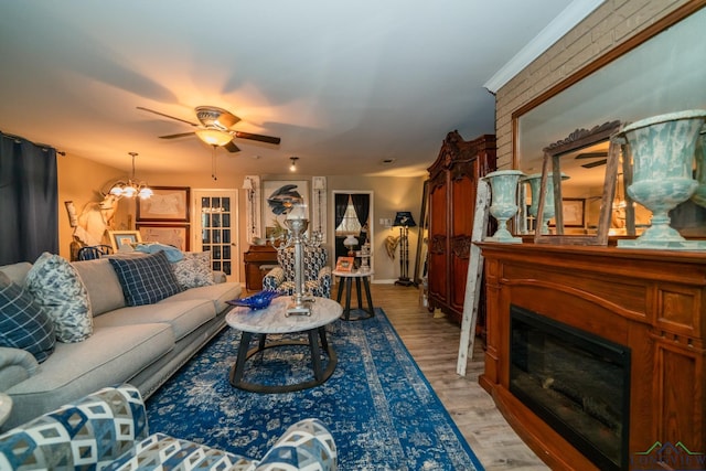 living room featuring a fireplace, ceiling fan with notable chandelier, and light hardwood / wood-style flooring