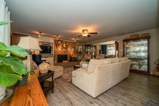 living room with hardwood / wood-style floors, ceiling fan with notable chandelier, and a brick fireplace