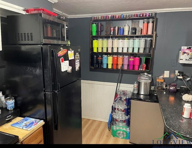 kitchen with wood walls, black refrigerator, crown molding, and light hardwood / wood-style flooring