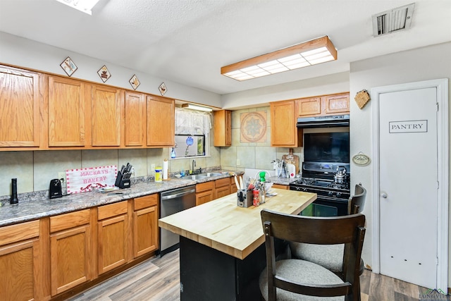 kitchen featuring stainless steel dishwasher, black range oven, backsplash, and light hardwood / wood-style flooring