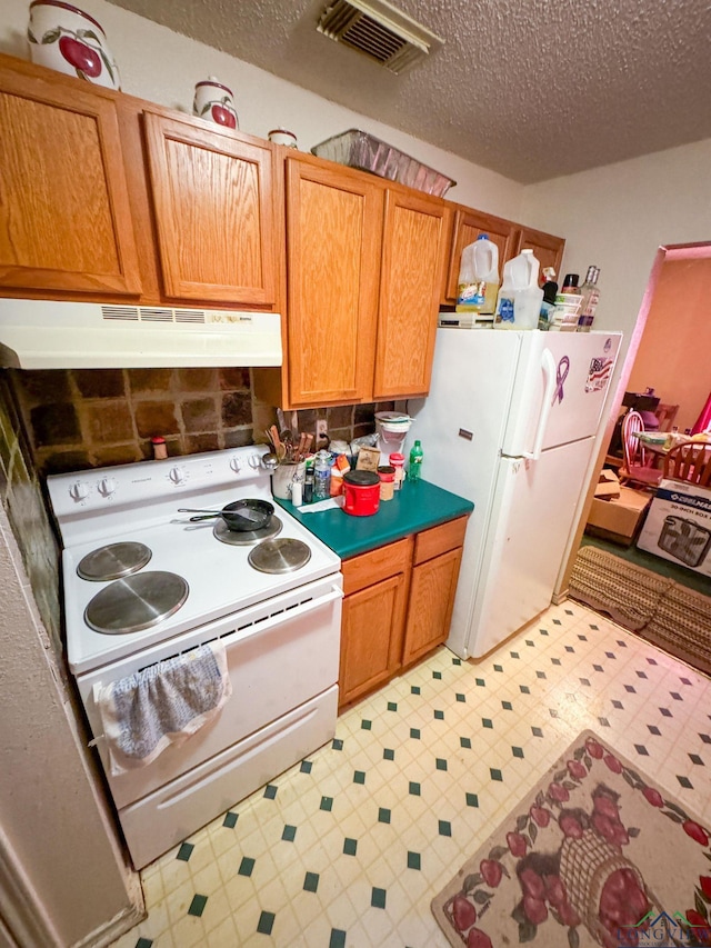 kitchen with a textured ceiling, under cabinet range hood, white appliances, visible vents, and light floors