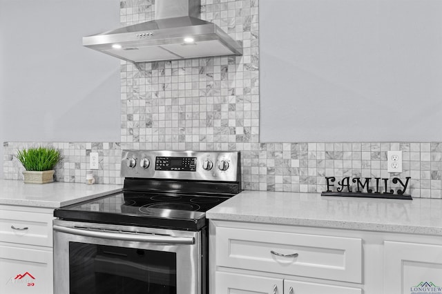 kitchen with electric stove, wall chimney range hood, decorative backsplash, white cabinets, and light stone counters