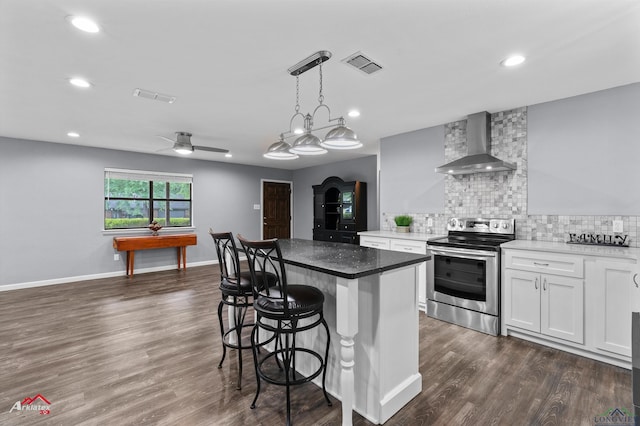kitchen with stainless steel range with electric stovetop, wall chimney range hood, tasteful backsplash, a breakfast bar, and a center island