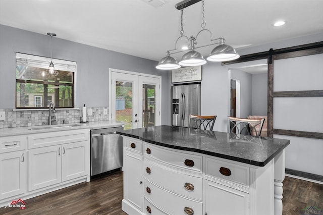 kitchen featuring stainless steel appliances, a sink, a barn door, dark wood-style flooring, and white cabinets