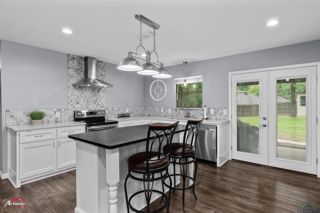 kitchen with wall chimney exhaust hood, stainless steel appliances, decorative backsplash, dark wood-style floors, and recessed lighting