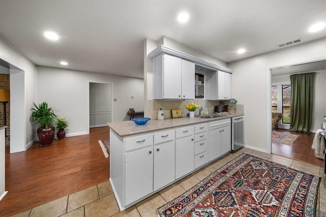 kitchen featuring tasteful backsplash, stainless steel dishwasher, sink, white cabinetry, and light tile patterned flooring