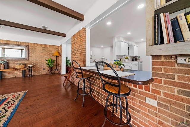 bar featuring beam ceiling, dark hardwood / wood-style flooring, white cabinetry, and brick wall