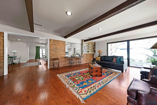 living room with beam ceiling, hardwood / wood-style floors, and brick wall