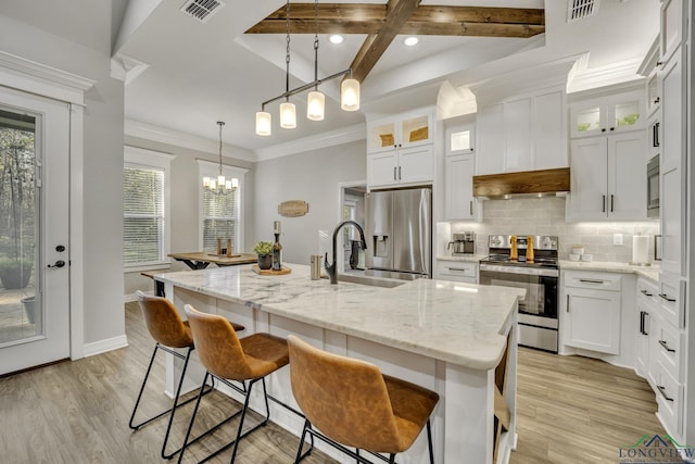 kitchen featuring white cabinets, beamed ceiling, pendant lighting, a kitchen island with sink, and appliances with stainless steel finishes