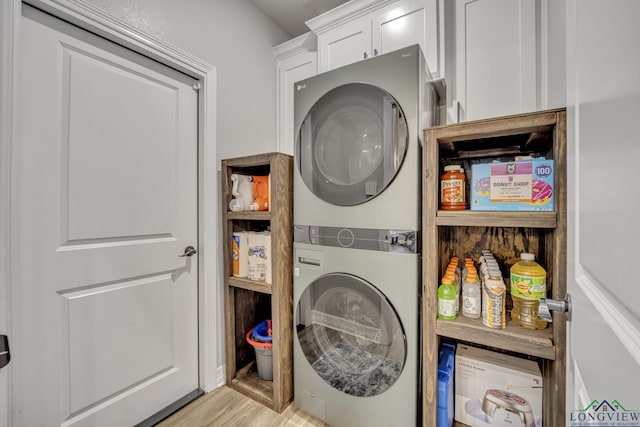 laundry area featuring stacked washer and dryer, light hardwood / wood-style floors, and cabinets