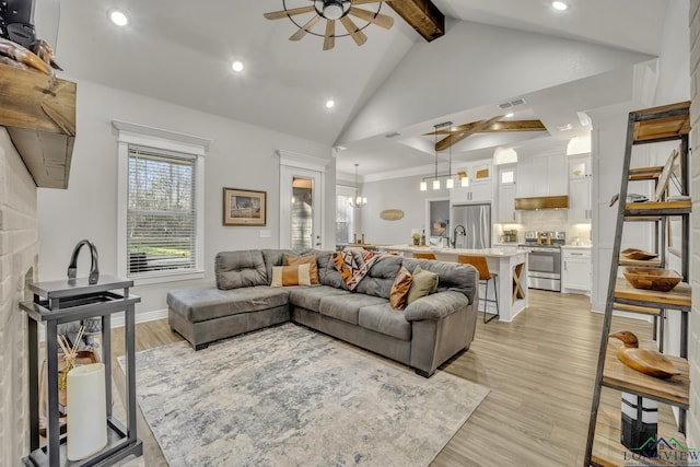 living room featuring light hardwood / wood-style flooring, high vaulted ceiling, beam ceiling, ceiling fan with notable chandelier, and sink